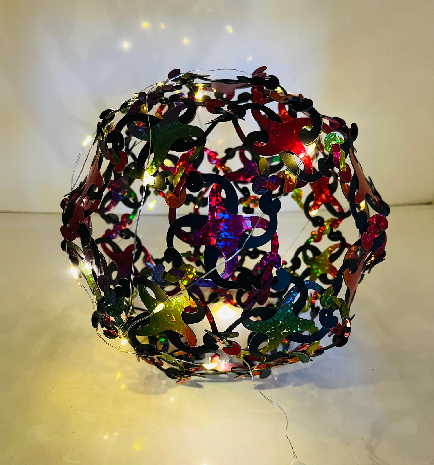 Boule ajourée en pièces holographiques multicolores, éclairée de l'intérieur par une guirlande lumineuse